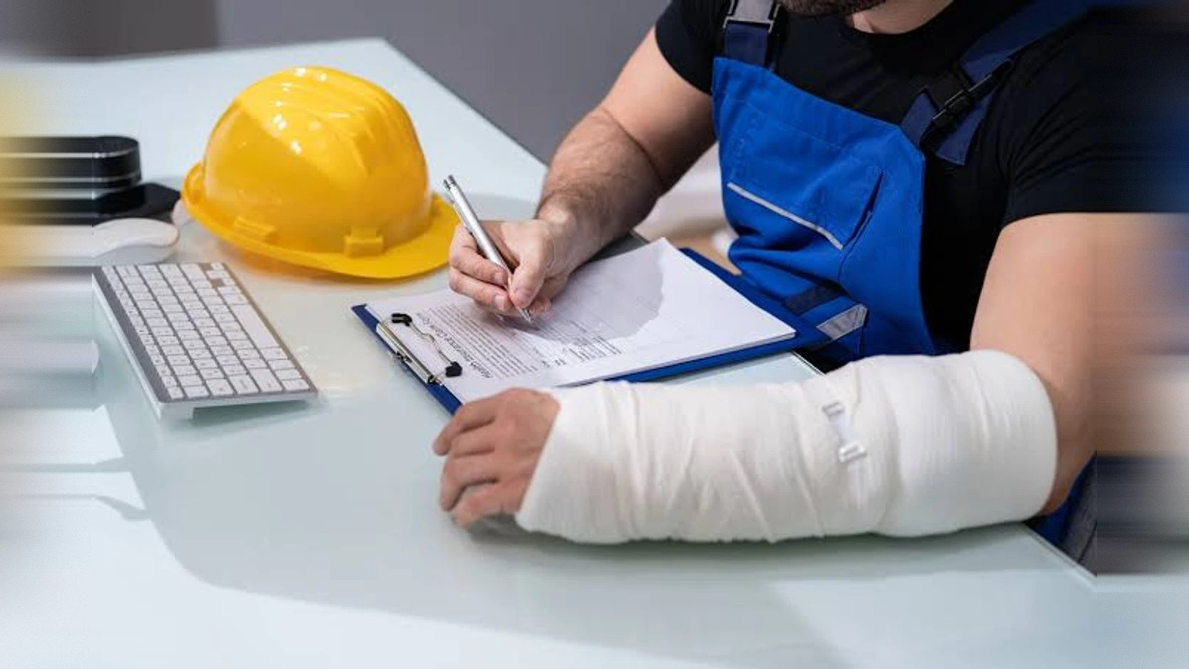 Trabajador con el brazo enyesado firmando un formulario junto a un casco de seguridad