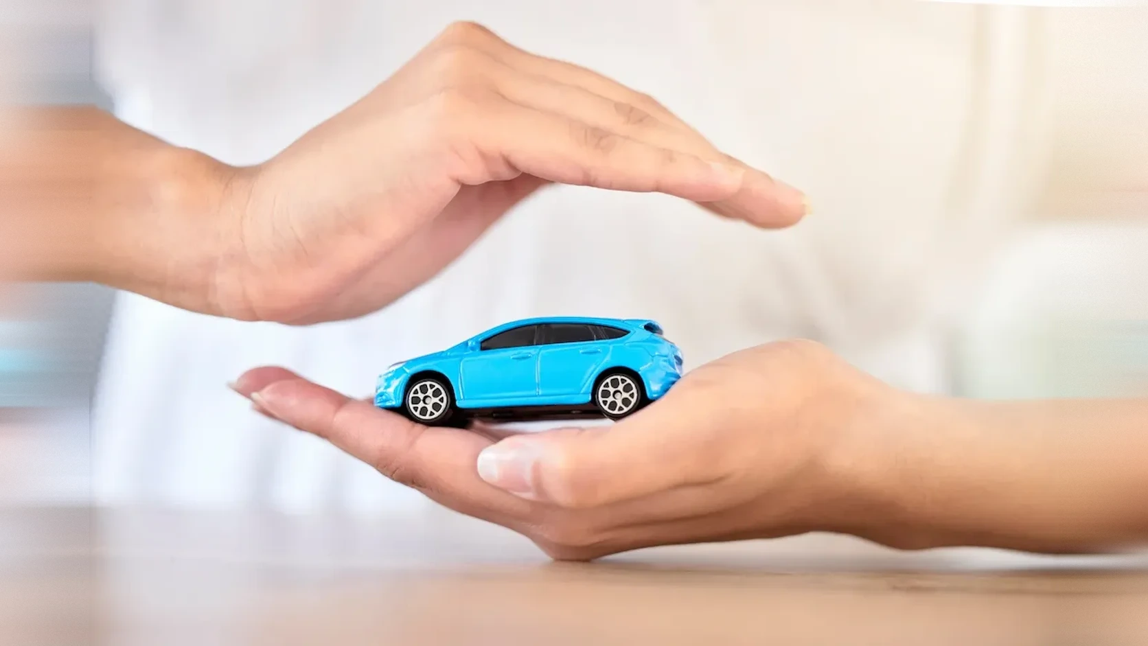 Manos protegiendo un carro de juguete sobre una mesa